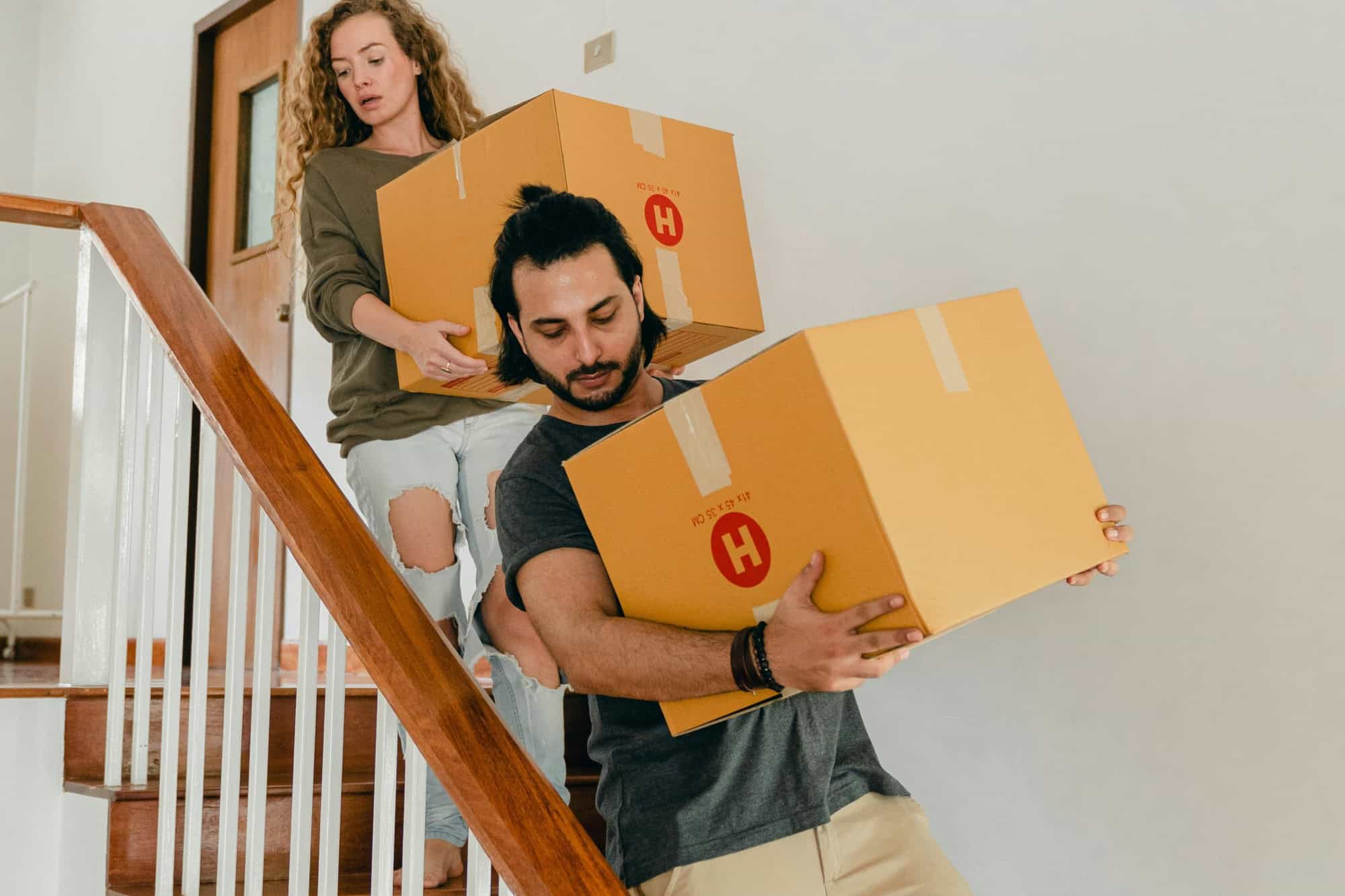 A couple is climbing down the stairs while carrying cartons in the concept of moving into Streatham.