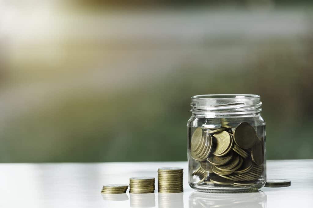Coin stack and coins inside a glass jar in the concept of saving money for the move to Streatham.