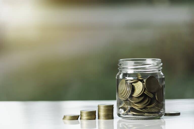 Coin stack and coins inside a glass jar in the concept of saving money for the move to Streatham.