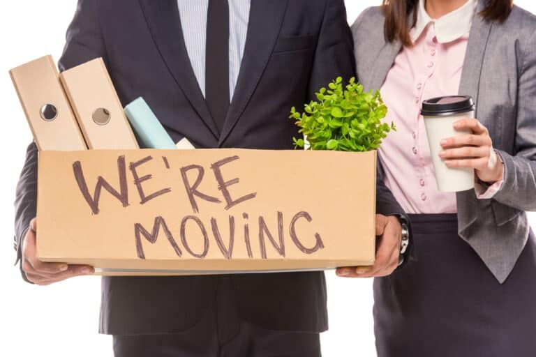 Cropped image of two employees holding a carton of their office items with a text ' We're Moving' in the concept of 'How to Plan and Coordinate an Office Move in Streatham'.