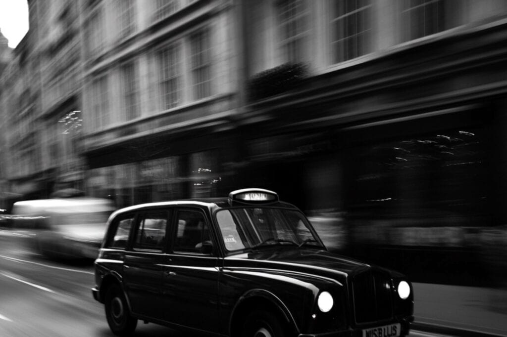 Black-and-white photo of the iconic black cab speeding on a street with a blurry background